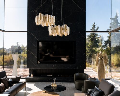 Πολυτελές minimal καθιστικό διπλού ύψους με γωνιακά κουφώματα αλουμινίου, μαύρη μαρμάρινη επένδυση και μεγάλες υαλώσεις σε σύγχρονη ιδιωτική κατοικία.